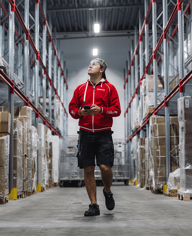 Medarbetare på åkeriets lager, håller mobil och kollar lagret.